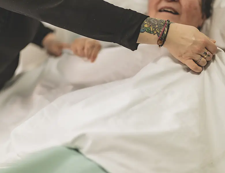 Due mani amorevoli rimboccano le coperte ad una paziente della fondazione Gigi Ghirotti di Genova.