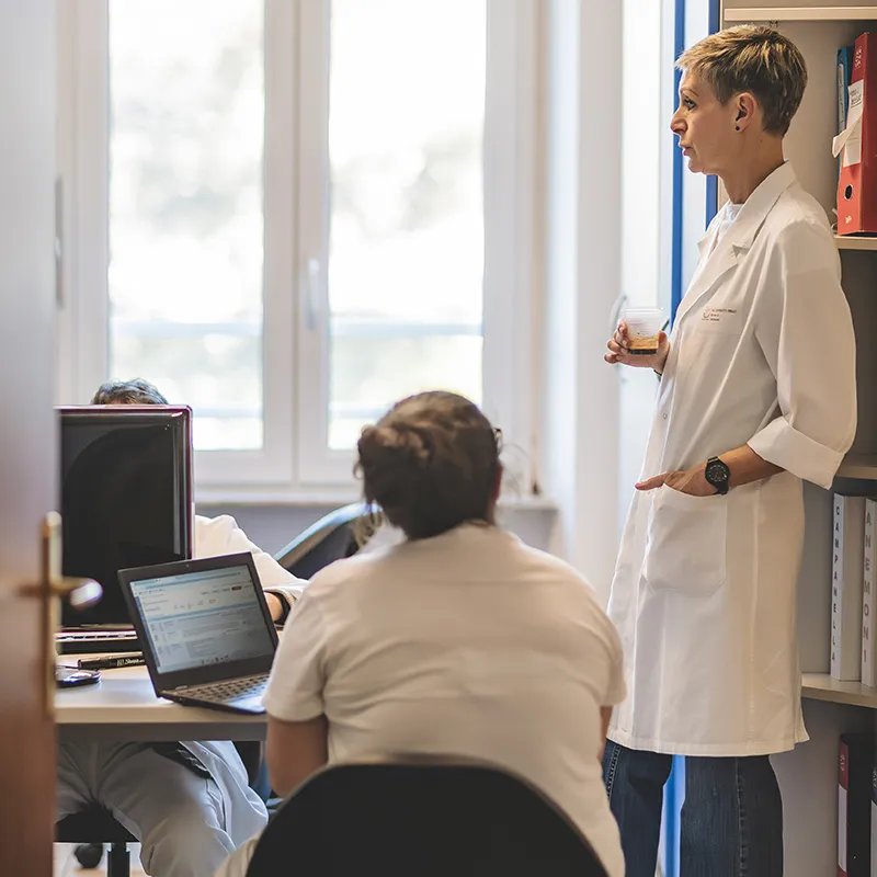 Tre medici a consulto in uno studio medico, due sono seduti ad una scrivania mentre una terza dott.ssa è in piedi vicino a loro.