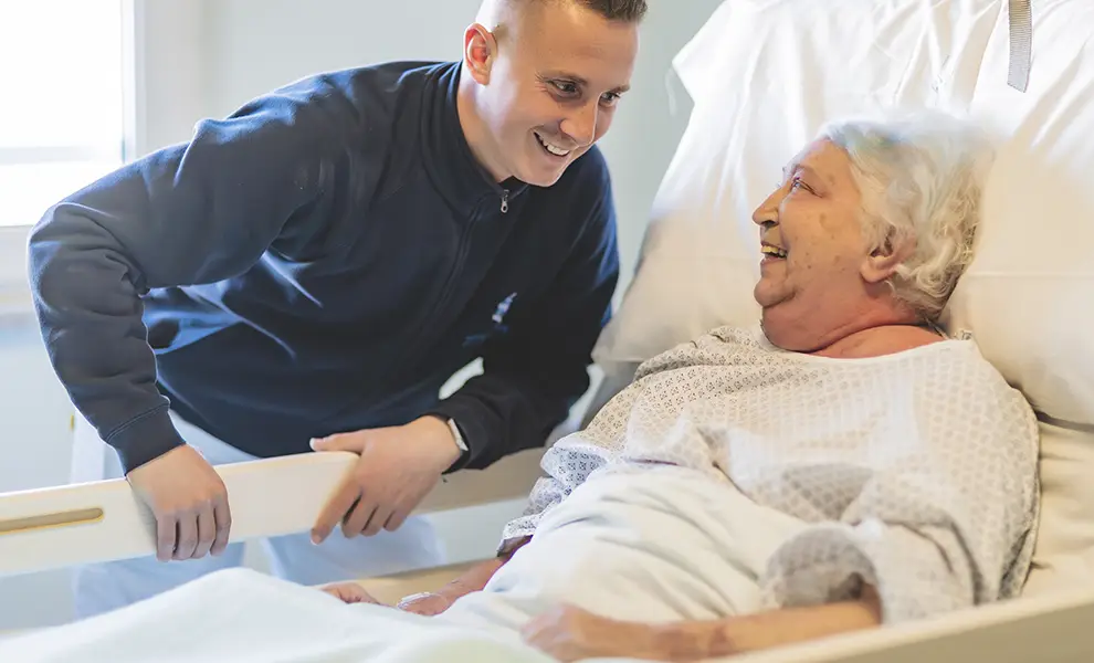 Volontario della fondazione Gigi Ghirotti sorride e conversa amabilmente a diretto contatto con una paziente a letto in uno degli hospice.