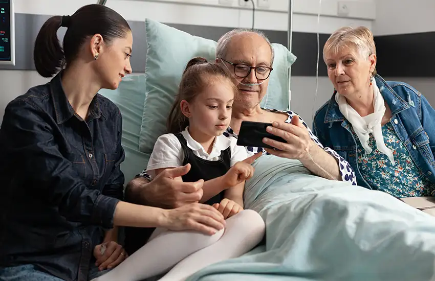 Nonni con figlia e nipotina guardano un video sul letto del nonno malato, ricoverato in uno degli hospice della fondazione.