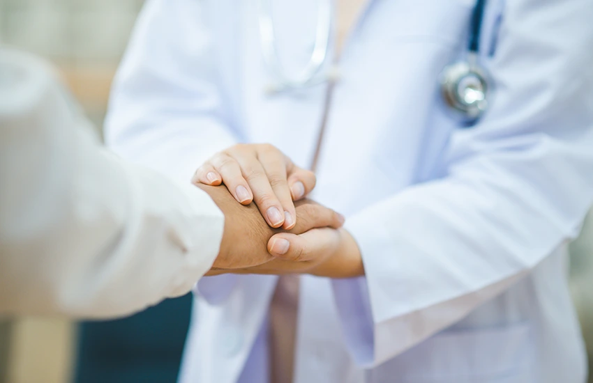 Un medico tiene le mani di un paziente. Le due figure si vedono con focus sulle mani, mentre i volti non sono visibili