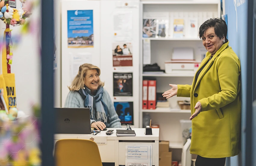 Interno dell'infopoint della Fondazione Gigi Ghirotti. Si vedono due volontarie che parlano amichevolmente