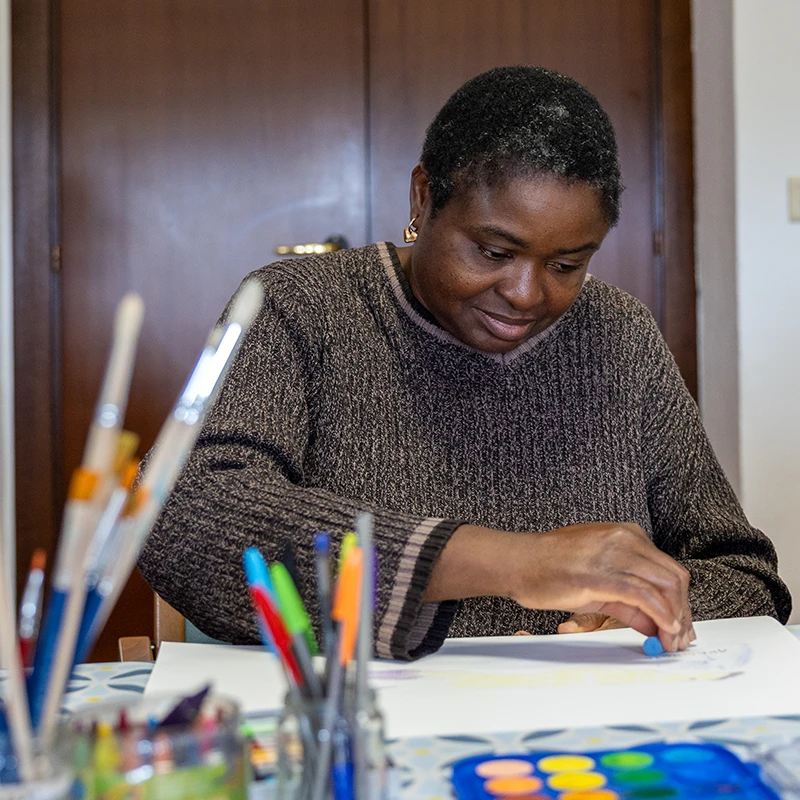 Una signora dedita ad attività di disegno, su un tavolo pieno di colori a disposizione.
